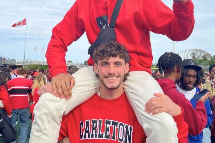 young male student standing holding another male student over his shoulders at a game